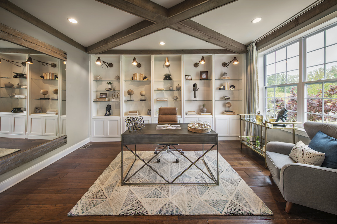 An organized home office featuring built-in shelving, beam ceiling, and mirror wall