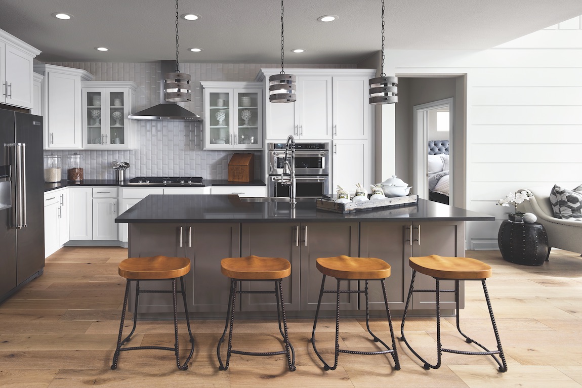 Kitchen with white cabinets, light wood flooring, brown wood bar stools and black island.