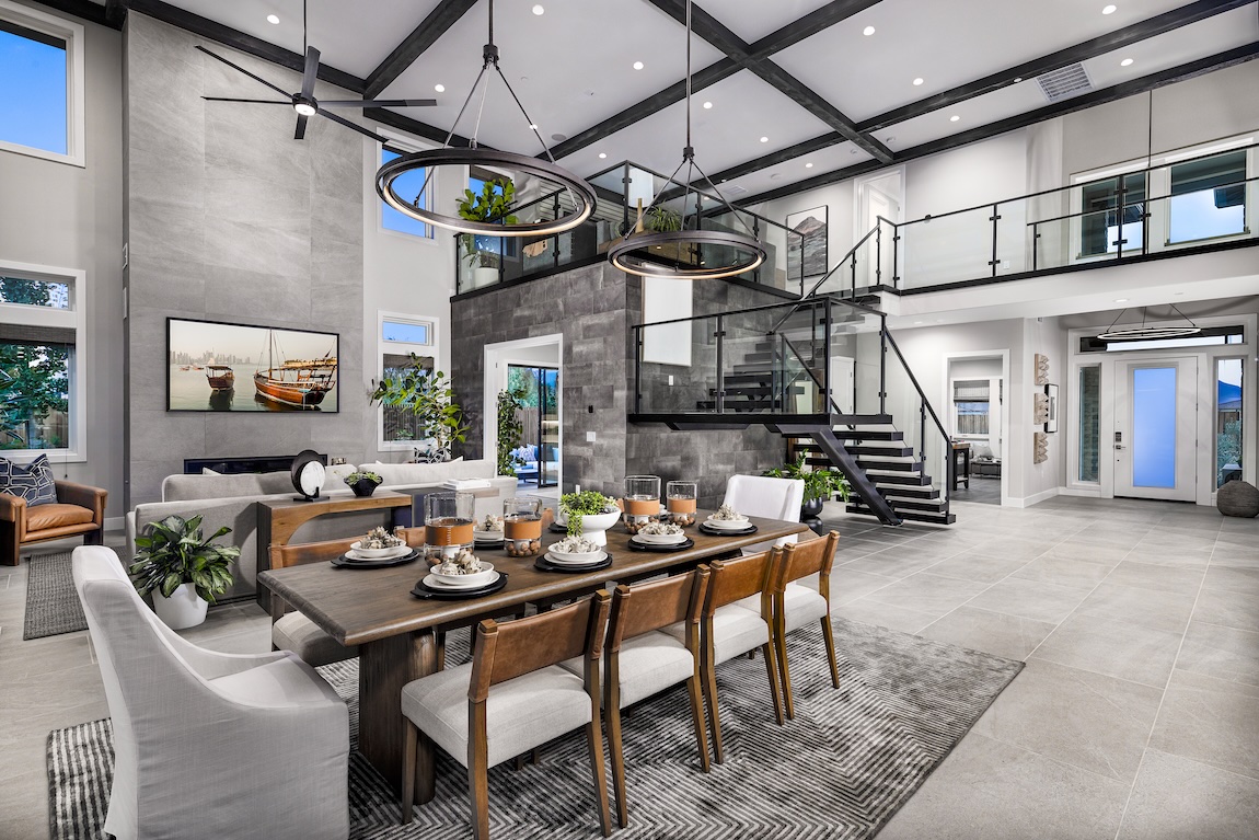 Contemporary staircase with glass railing in an open-concept luxury dining and living space featuring exposed beams, statement lighting, and modern finishes