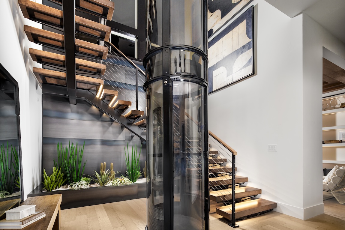 Modern floating staircase with under-step lighting beside a sleek glass elevator in a contemporary home entryway with indoor succulent garden