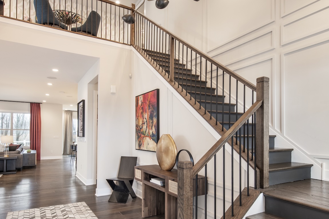 Wood staircase with black spindles and dark-stained treads in a modern foyer featuring paneled walls, abstract art, and open-concept living space