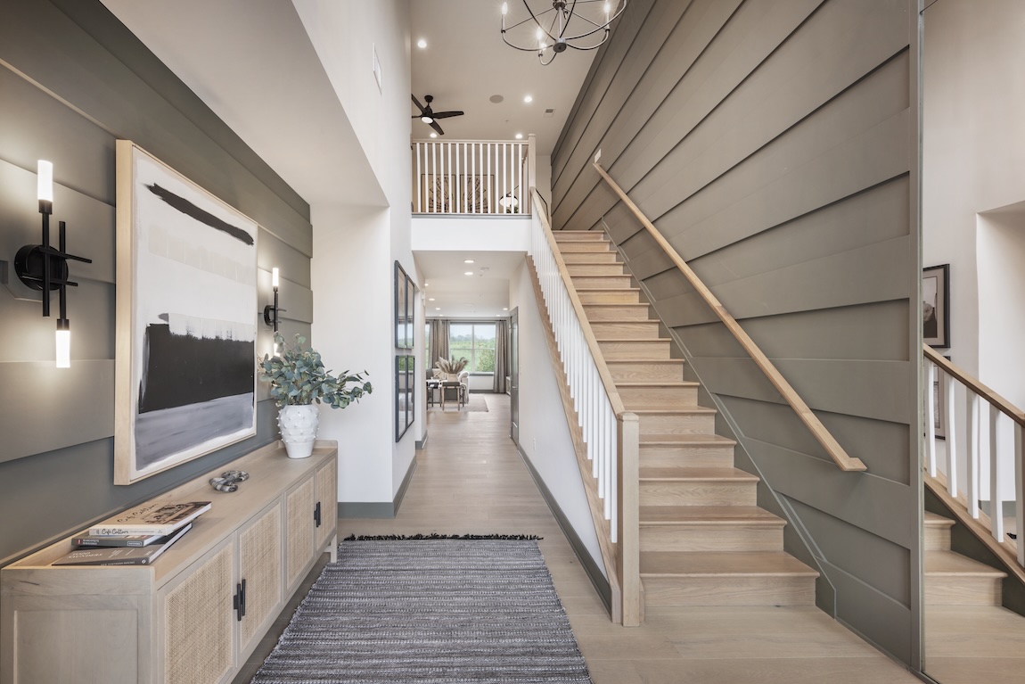 Modern wood staircase with white spindles in a neutral-toned foyer featuring shiplap accent walls, abstract artwork, and contemporary lighting