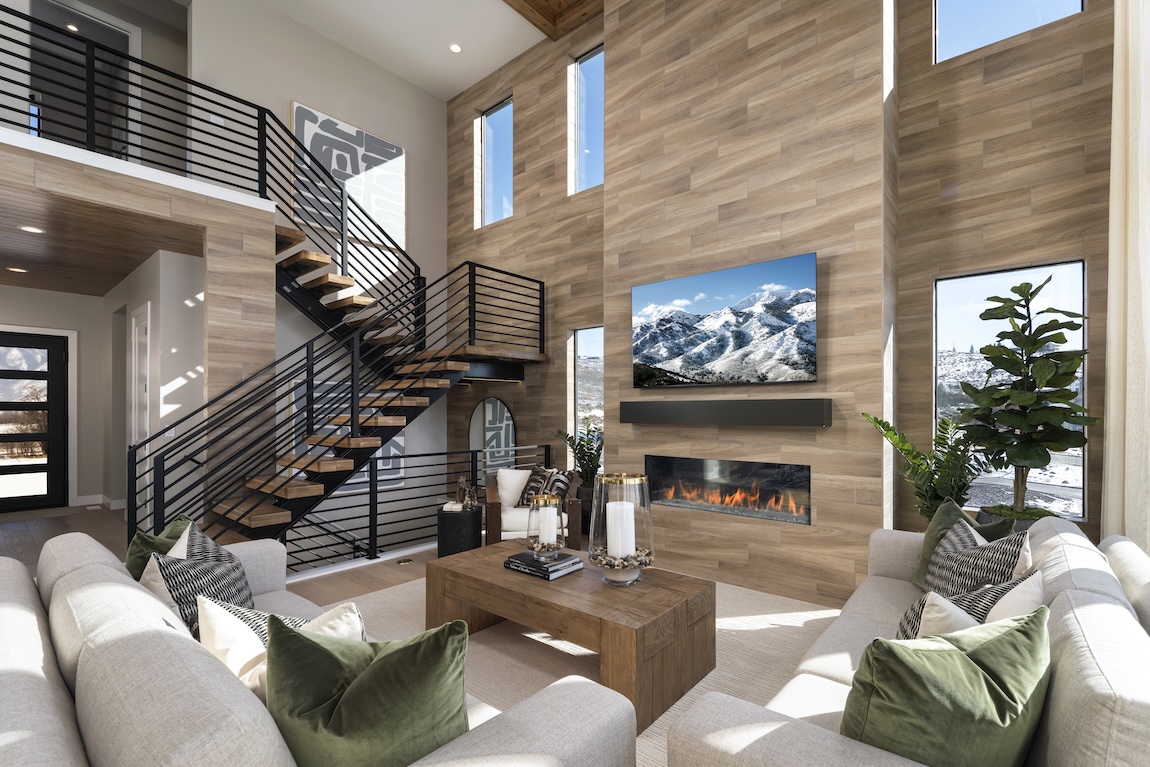 Contemporary wood staircase with black metal railing in a cozy great room featuring wood panel walls, fireplace, and mountain views