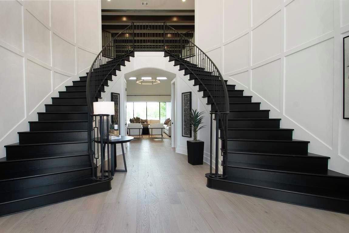 Dramatic dual staircase with black wood treads and wrought iron railings in a grand foyer with paneled white walls and arched entryway