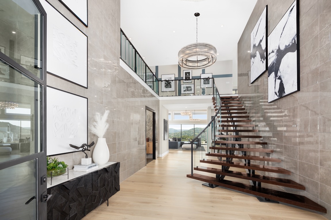 Floating wooden staircase with glass railing in modern luxury home foyer featuring large abstract art and double-height ceilings