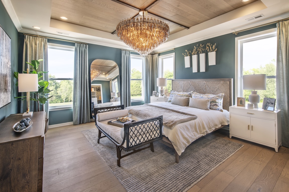 Green primary bedroom with luxe decor elements including freestanding mirror, chandelier, and accent ceiling