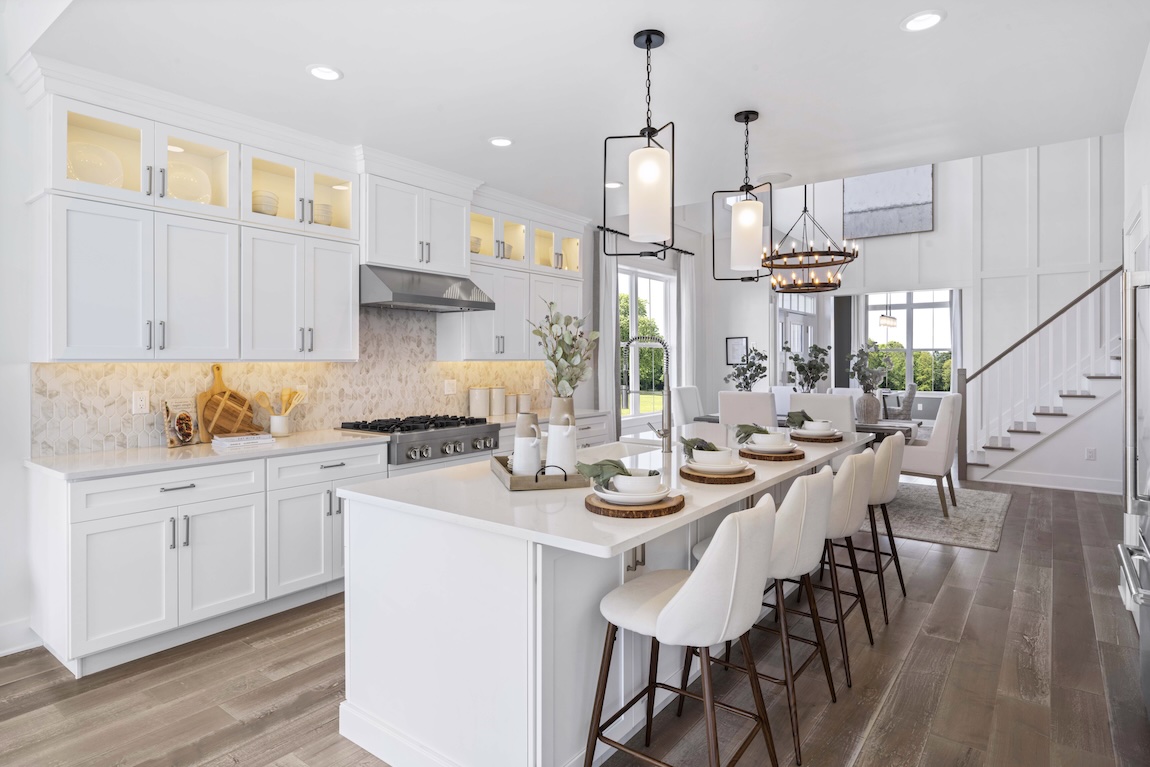 Modern open-concept kitchen and dining room with white cabinetry, quartz countertops, pendant lighting, high ceilings, hardwood floors, and a large kitchen island with bar seating - luxury home interior design