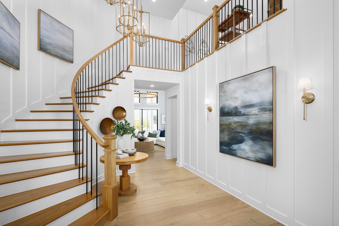 Curved wood staircase with black balusters anchors a bright foyer with white paneling and modern coastal décor.