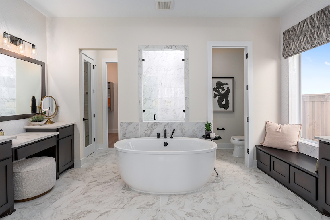 Modern freestanding tub in a marble-tiled bath with dual vanities and sleek black fixtures.