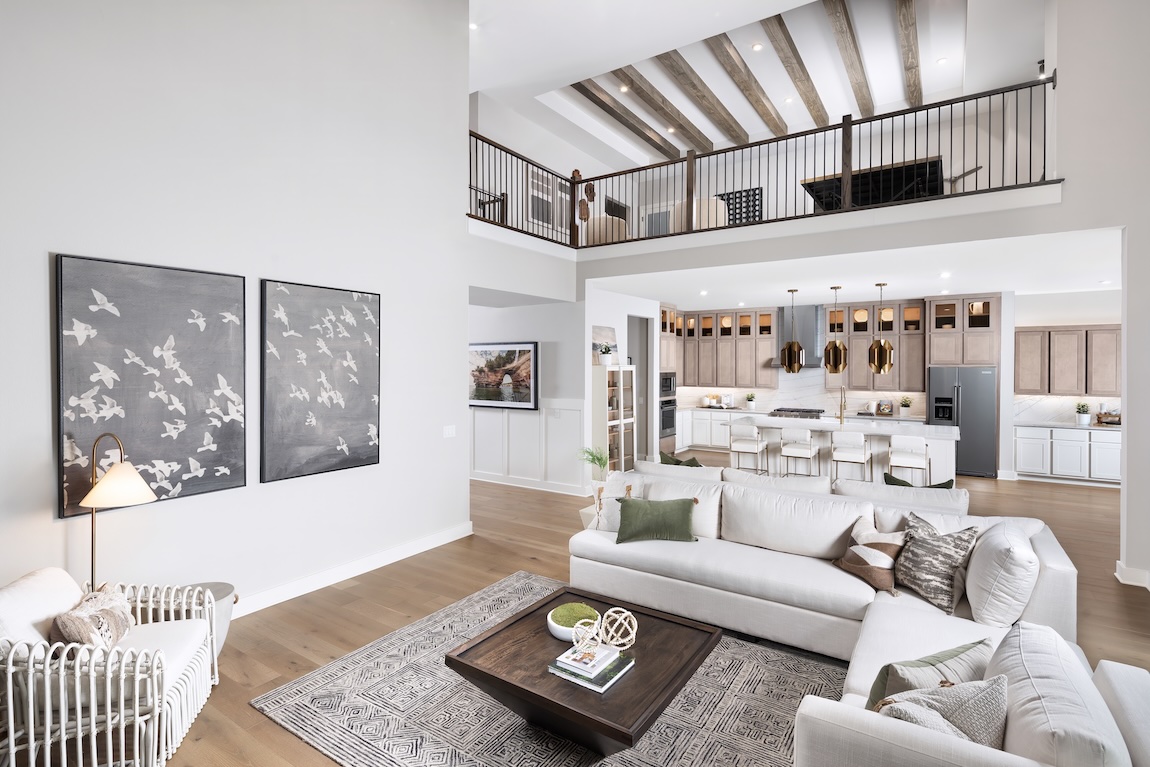 Modern open-concept great room with loft, wood beams, and seamless kitchen connection.