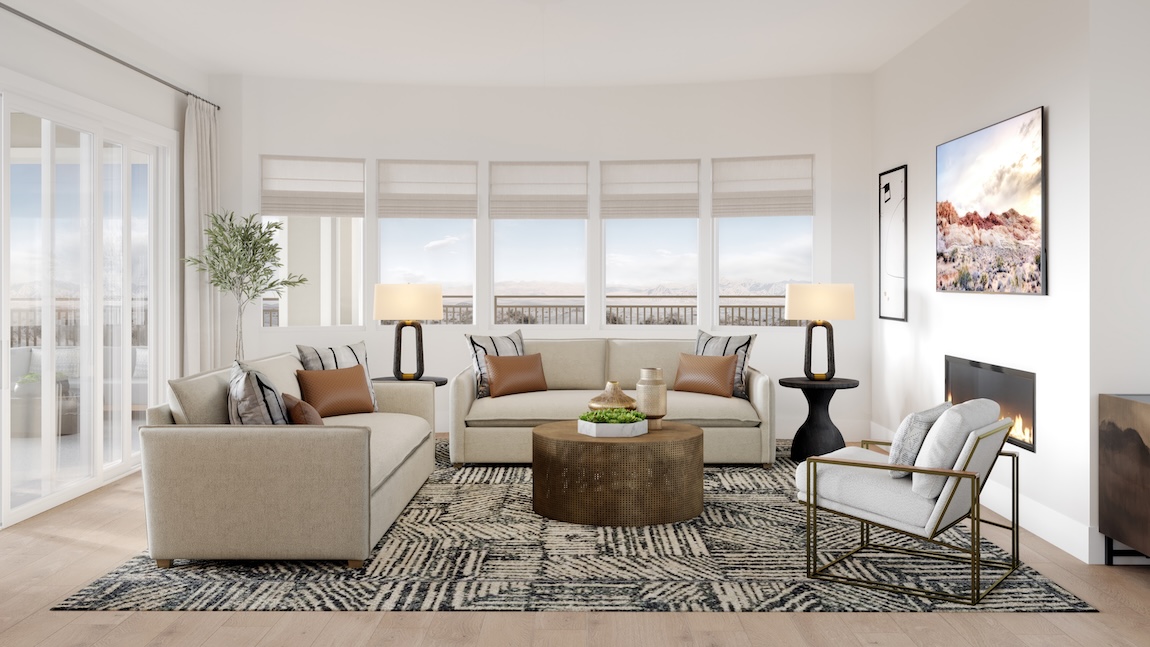 Warm transitional great room with neutral sofas, round wood coffee table, patterned area rug, large windows, and soft layered textures.