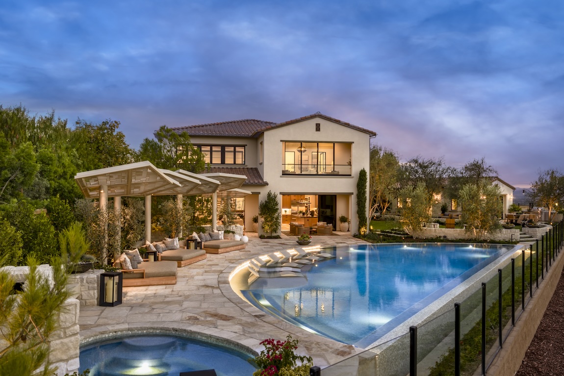 exterior of home with warm interior lighting and pool